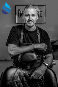 Black and white photo of a barber and SMP artist standing behind a barber chair.