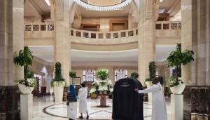 two guest walking in the lobby of Makkah Clock Royal Tower, A Fairmont Hotel with bellhop behind with bag cart
