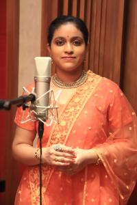 Lovely South Indian Singer in an apricot-colored sari standing with a microphone.