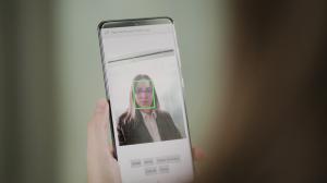 Image of a woman using her mobile phone for secure biometric identification using facial recognition. "Face Verification 13.0 from Neurotechnology is designed for the integration of high-quality face capture, secure facial authentication and robust face l