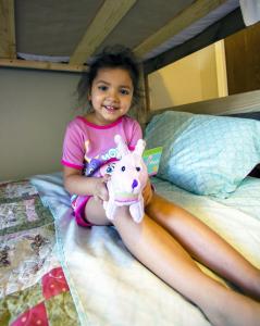 child sitting on their own new bed with a stuffed animal