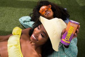 Two women laying on the ground holding a can of SUNBOY Spiked Coconut Water