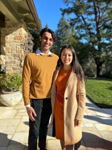 Photo of the co-founders of Capd Period and creators of CapdCup: Hannah Wilen, founder and CEO, and Neil Bhatia, co-founder and COO. Neil is standing on the left in a yellow mustard sweater, and Hannah is standing on the right in an orange dress and beige
