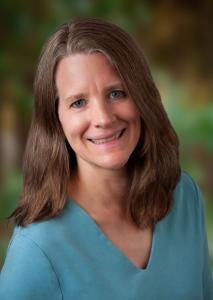 A headshot of Sydney Dunlap, a caucasian woman in her 40s with light brown hair and blue eyes. She is wearing a teal shirt.