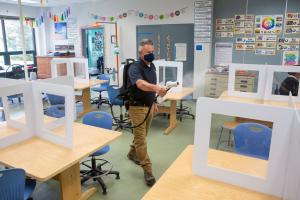 A man wearing a face mask sprays disinfectant in an empty school classroom.