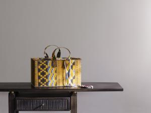 Glass sculpture made to look like a woven fabric handbag sits atop wooden console
