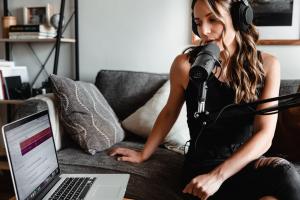 A picture of a podcaster recording a podcast with their microphone and laptop set up from their couch.