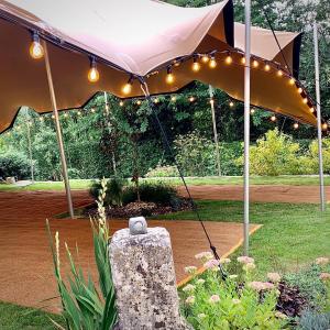 Image of a sand-colored 10m x 15m stretch tent, a popular choice for outdoor events and weddings in France. The tent is made of high-quality stretch fabric that is durable and weather-resistant. The stretched tent has festoon hung around the sides 