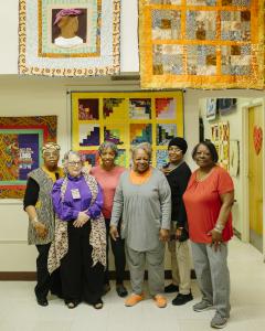African American women stand in front of a quilt