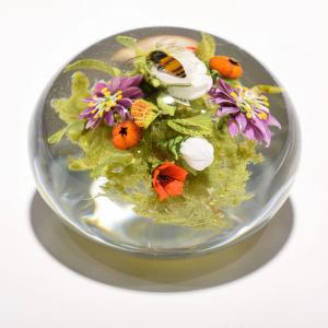 A glass bubble with tiny sculptures of plants and a bumble bee inside.
