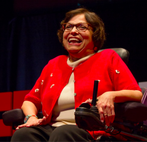 Judy Heumann wearing a red suit jacket and glasses