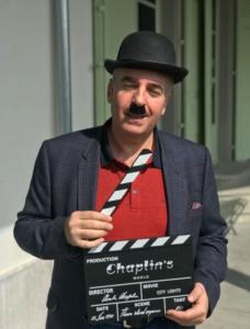 Kassem Lahham posing Charlie Chaplin with a clapboard and Charlie's iconic mustache