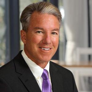 Profile picture of Dr. Lowney wearing a black blazer, white shirt, and a purple tie