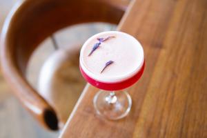 Looking from overhead at a magenta-colored cocktail with egg white foam and finished with purple dried flowers