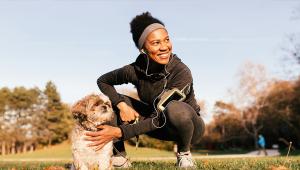 A woman squats down to pet her dog at the park