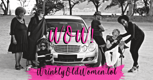 On a beach with a mercedes. 6 WOW! Wrinkly Old Women. 3 on the left. 1 with head phones. 1 look down at a book and sitting on the sand readying. 3 on the right. 1 with a hat leaning against a car. One sitting in a beach chair knitting and the other stoopi