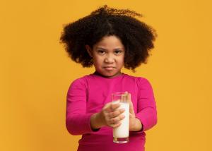 A Black child reacts negatively to a glass of milk.