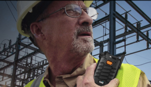 Image shows a middle-aged working man in a hard hat in front of an electricity substantion. He has a TAIT AXIOM Wearable communications device clipped to the left-hand side of his chest.