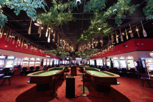 A photo taken down the middle shows the casino of the Temporary, with a dark ceiling that is decorated with fake pine leaves and vertically hanging canoe paddles that are painted with intricate native-inspired designs. The carpet is a deep red and in the