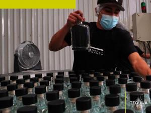 A man holding mezcal bottles, working at a mezcal distillery in Oaxaca Mexico that produces mezcal private brands