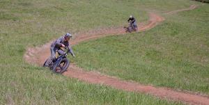 two bike riders on electric bikes riding on a singletrack trail