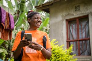A portrait of Solar Sister Entrepreneur Agnes Timothy Sarakikiya, Tanzania holding her smart phone.