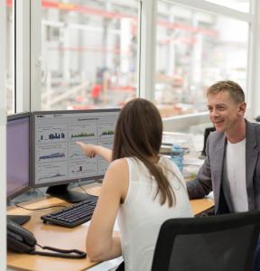 Two employees at a desk, looking over dashboards on a computer screen