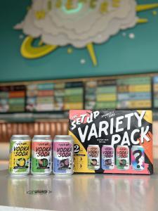 A colorful box labeled The Set Up Variety Pack is on a counter with 12-ounce beverage can next to it in front of a teal wall.