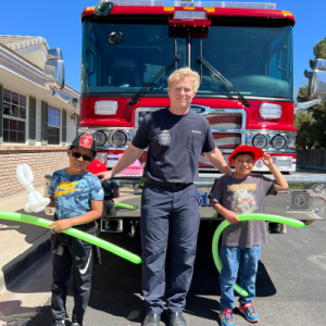 Gilbert Fire & Rescue team member in front of rig with two boys during community event