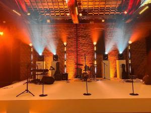 A large white stage with lighting, sound equipment & microphones for a live wedding band