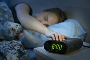 A sleepy woman in bed, reaching out to turn her alarm clock off