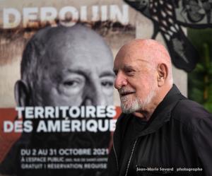 photo of the face of artist René Derouin in front of a banner advertising the Lands of the Americas fulldome project created about his artwork.