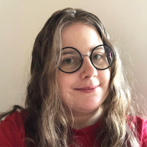 Portrait photo of a smiling young white woman with long light brown hair and round black-rimmed glasses.