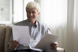 Happy satisfied elder retired bank customer man reading paper document