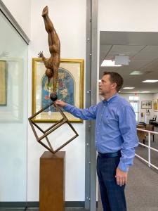 man inspects a tall bronze sculpture of an acrobat doing a handstand