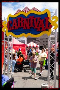 Image includes Carnival Sign, person in a wheelchair, childe with a prize, balloons, carnival tents, and Michelle Heart as Black Widow from the Treasure Valley Avengers