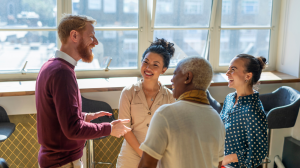 Several people from diverse backgrounds standing together in a room, conversing and smiling.