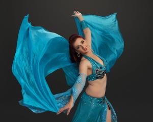 Photo of a belly dancer in a blue costume with a matching blue veil swirling behind.