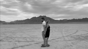 a black and white still image of actor Ray Dwyer Jr. and actress Shaun Rylee from the experimental short film, You Don't Deserve This. They are standing back to back in the middle of the desert.