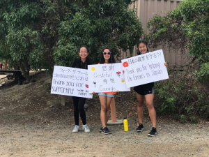 Three OCO Club volunteers holding signs along the walking path that read, "Thank you for supporting Walk the Farm." "Grateful. Courage." and "Thank you for helping the farmers in Japan" in English and Japanese. greeting the walkers at Walk the Farm
