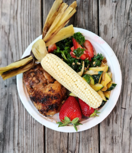 Farm-to Table Cookout Tour plate with fire-grilled Smokehouse Maple Chicken, Roasted Corn on the Cobb, Signature Kale and Strawberry Salad, grilled veggies, and fresh strawberries for dessert..