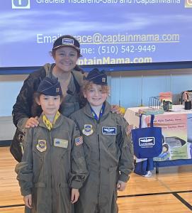 Graciela Tiscareno-Sato, Captain Mama, at bilingual schcool assembly with 2 girls dressed as Captains of their lives wearing the Air Force veterans flight suits and posing like confident aviators