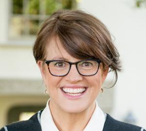 Photo of author, podcaster and PBS host Kelly Corrigan, a 56 year old white women with glasses and big smile.