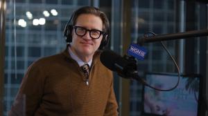 WGN Radio Host John Williams is show here in the studio. He is a 64 year old white man wearing a brown sweater and glasses.