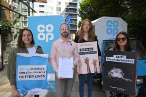Co-op members supporting the Better Chicken Commitment stand outside the AGM with placards and Co-op banners behind them.