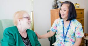A Home Care patient is greeted by a Home Care nurse at her home. The two women are smiling.