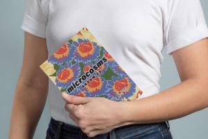 Person in white t-shirt holds book in left hand, against their body.