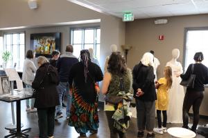 A crowd of visitors gathers around a stunning display of robe and gown toiles. They are captivated by the intricate details and exquisite craftsmanship of the garments. 