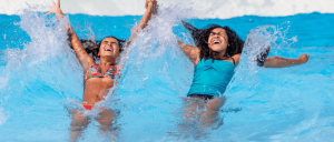 young girls playing in the water with eyes closed as waves hits their backs