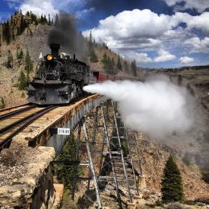 A black locomotive crosses a trestle with steam billowing.